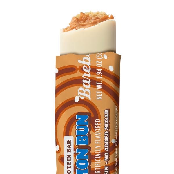Barebells Cinnamon Bun protein bar unwrapped, showing white chocolate coating with cinnamon bun-flavored crispy topping