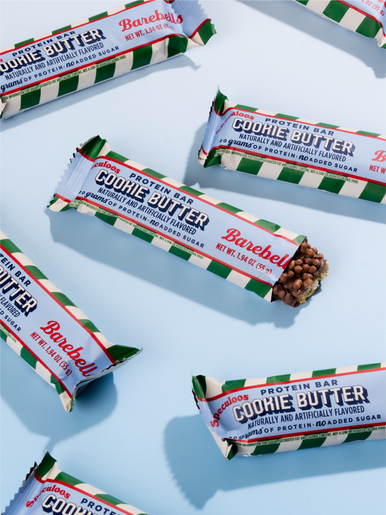 Multiple Barebells Cookie Butter protein bars with green and white striped packaging arranged on a light blue surface