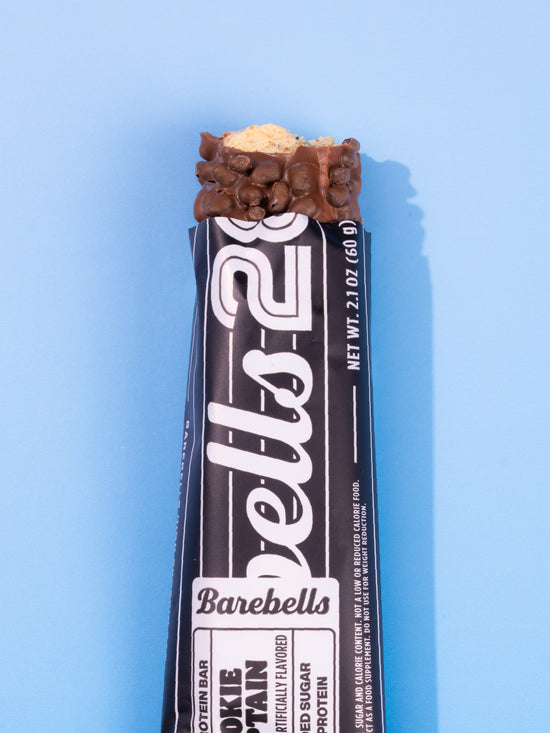 Barebells Cookie Captain protein bar with chocolate coating and cookie pieces on top against blue background