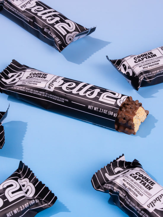 Barebells Cookie Captain protein bars with black packaging arranged on blue background, one bar unwrapped showing chocolate coating and cookie pieces
