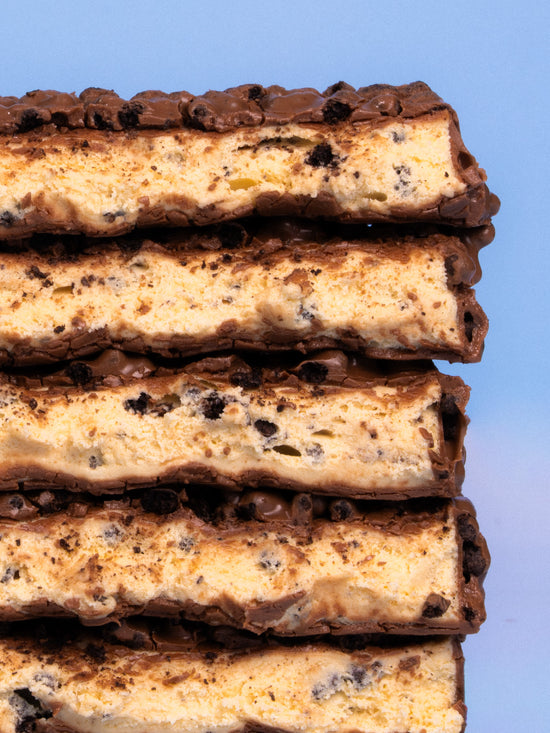 Stack of five Barebells Cookie Captain protein bars with chocolate coating and cookie pieces, shown in cross-section against blue sky
