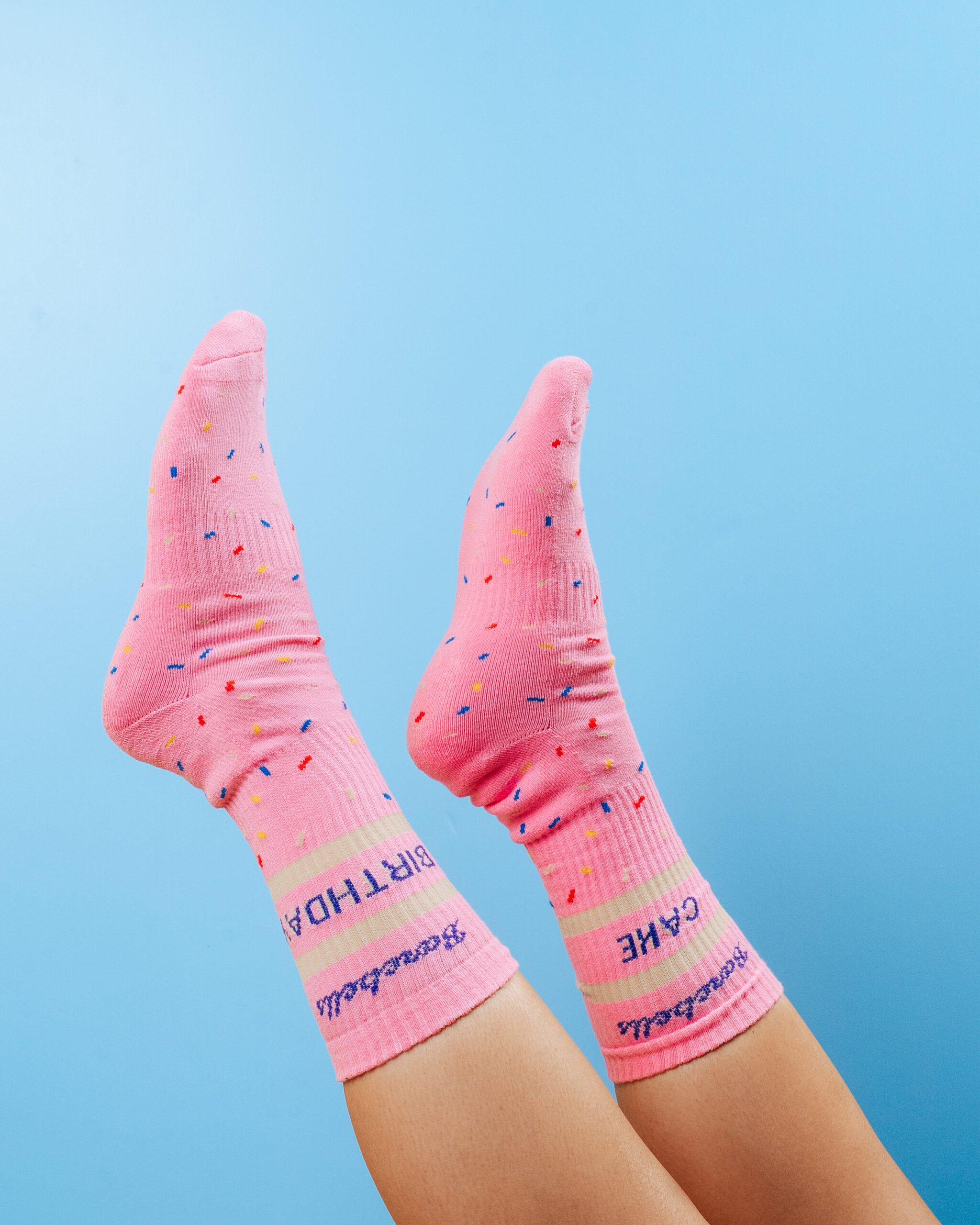 Pink socks with colorful speckles and text, raised feet against a blue background.