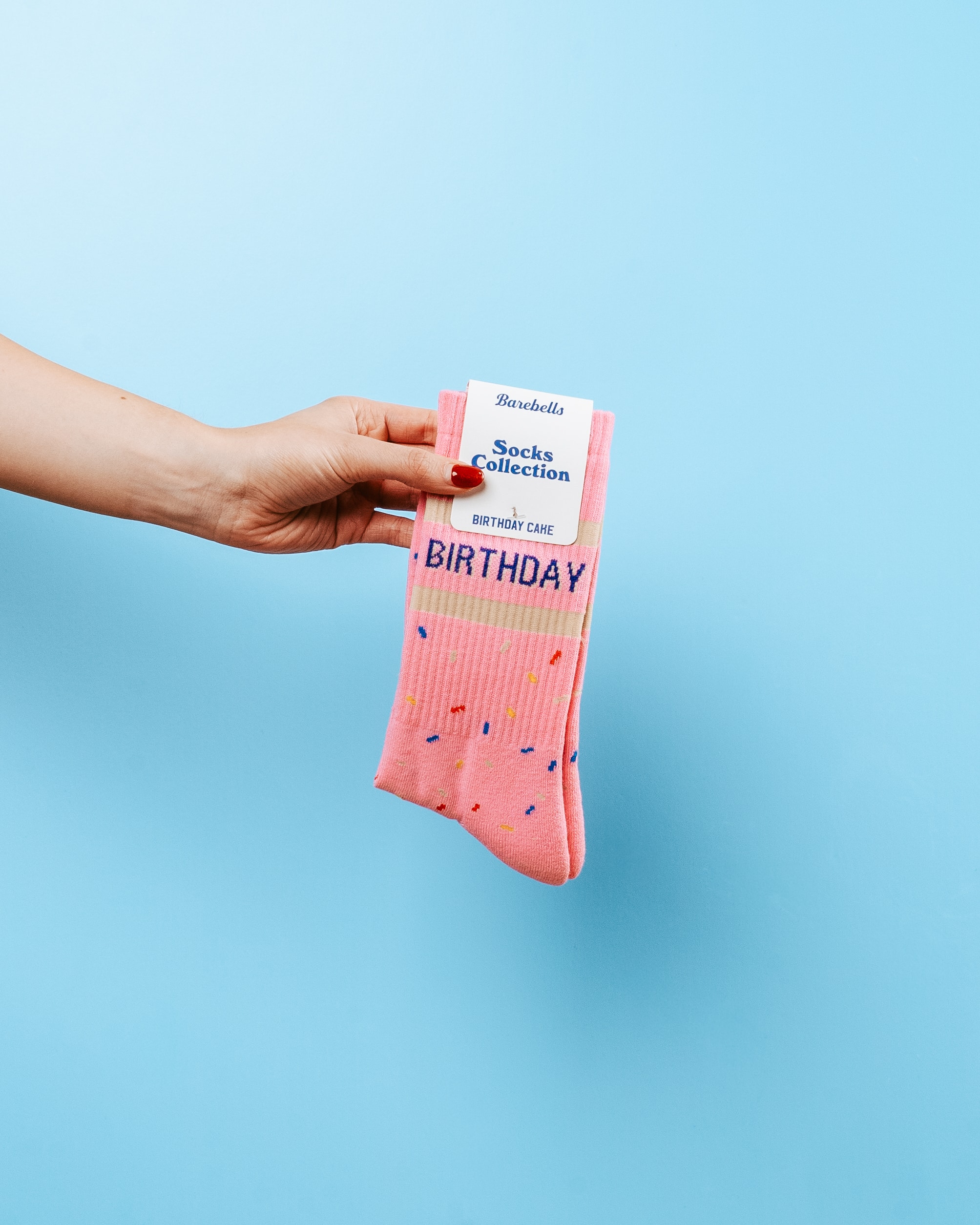 Hand holding a pair of pink birthday-themed socks against a blue background.